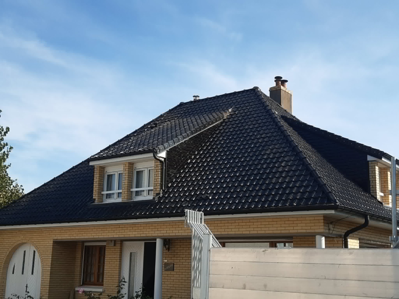 Maison en brique avec une grande toiture sombre terminée et deux fenêtres en façade.
